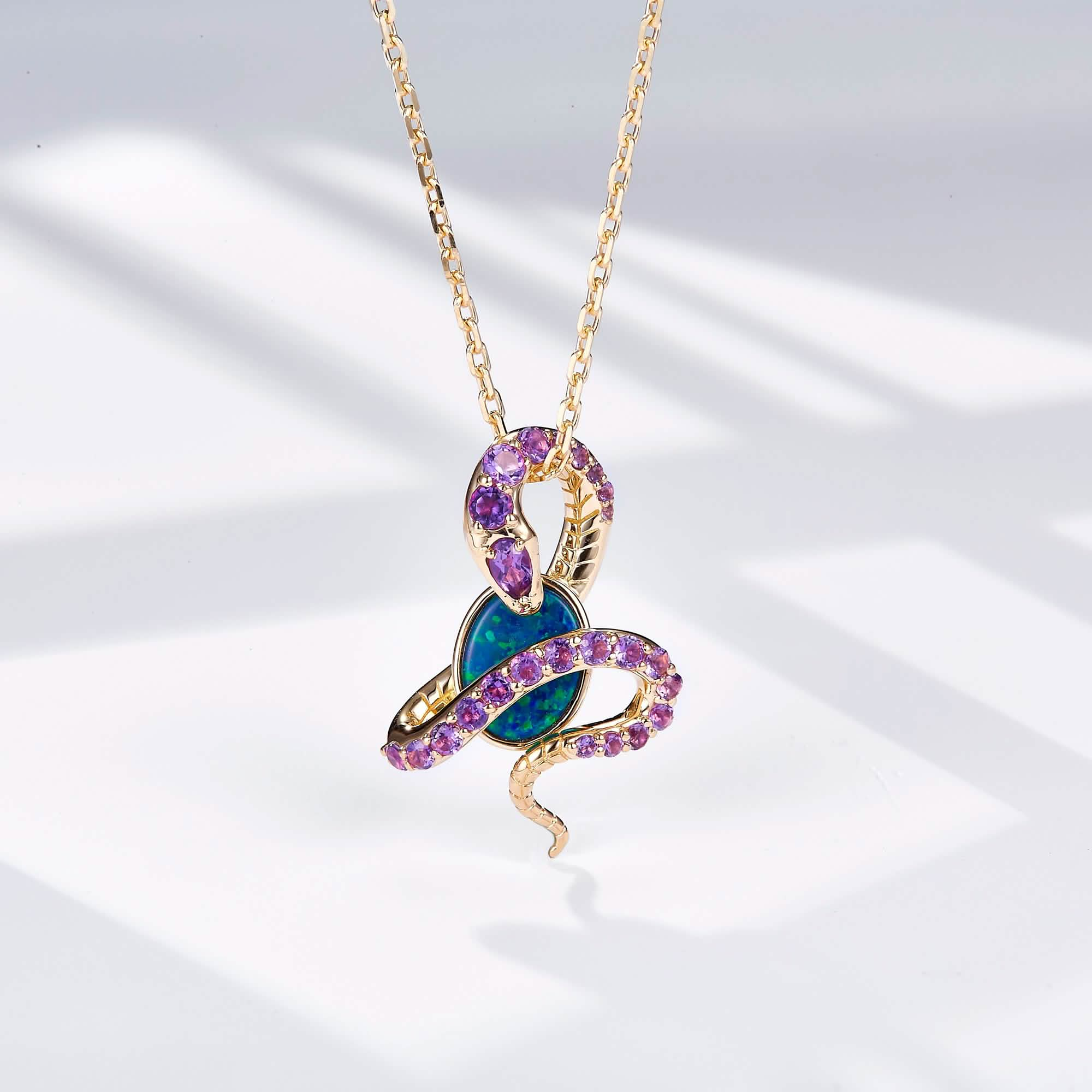 An 18K gold pendant necklace featuring an oval Australian opal wrapped in an intricate snake design adorned with natural amethyst gemstones. The opal displays vibrant blue-green hues, beautifully contrasted by the rich purple of the amethysts and the warm yellow gold setting. The pendant hangs from a delicate gold chain, creating a bold yet elegant statement piece.